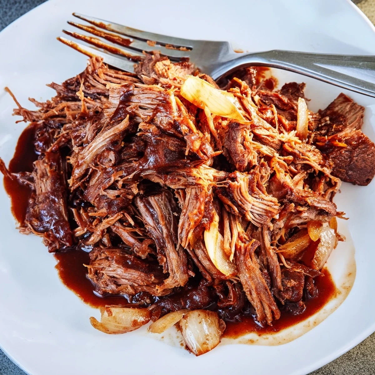 Slow Cooker BBQ Pulled Beef shredded fine and dripping with tangy sauce in a ceramic bowl