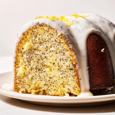 Freshly glazed Lemon Poppy Seed Bundt Cake with Glaze on a white plate, drizzled frosting dripping down the sides.