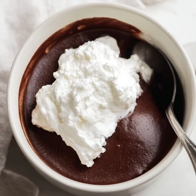Velvety chocolate pudding with homemade whipped cream, served chilled in individual dishes and ready for a chocolate shaving garnish. 