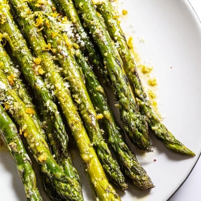 Fresh Lemon Garlic Roasted Asparagus arranged on a white plate with lemon zest and grated Parmesan.