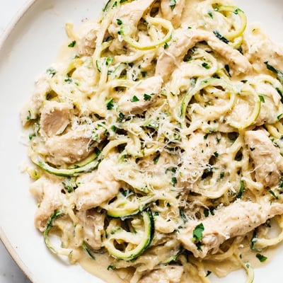 Slice of golden grilled chicken resting on a bed of zucchini noodles tossed in rich Alfredo sauce.
