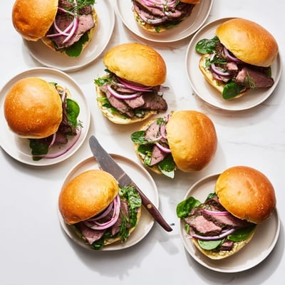 Soft slider buns holding tender beef slices topped with vibrant green arugula and onions.