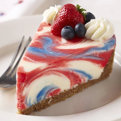 Slice of Patriotic Swirl Cheesecake topped with whipped cream and fresh berries