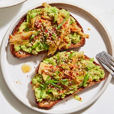 Kimchi avocado toast garnished with green onions and red pepper flakes on rustic bread